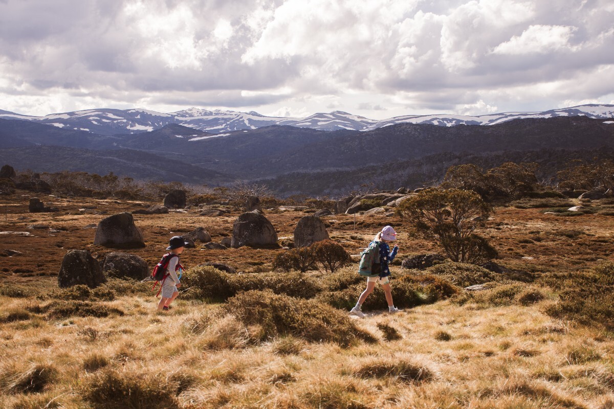 Young children walk on hiking trail in front of snow capped mountains