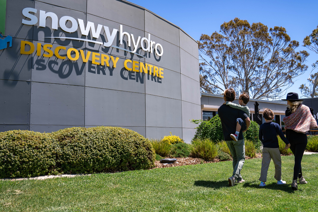 A young family wlk towards the entry to the Snowy Hydro Discovery Centre building