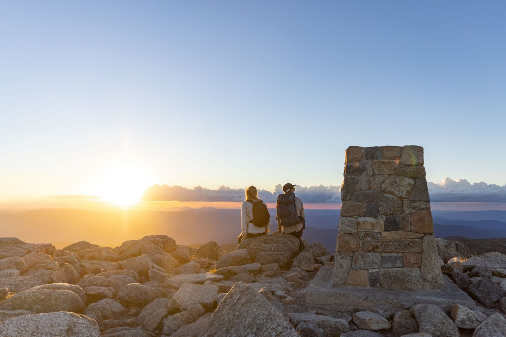 Two People sit on top of mountain looking at sunset
