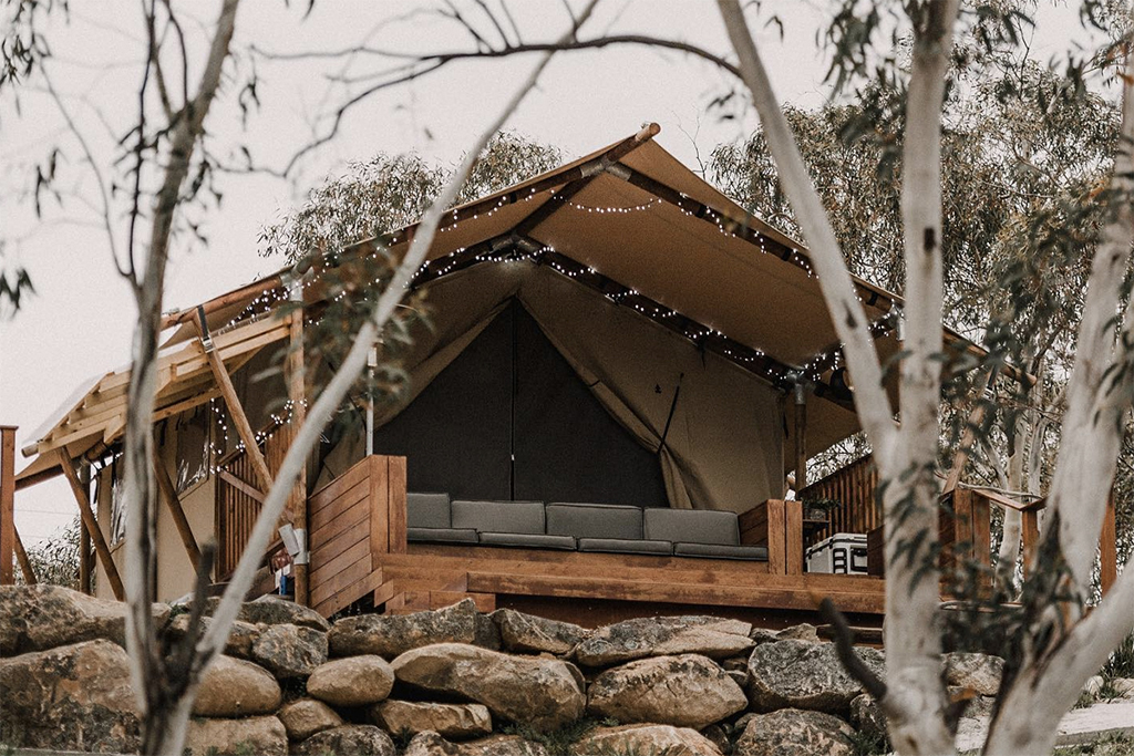 safari tent sitting on top of rock wall surrounded by bushland